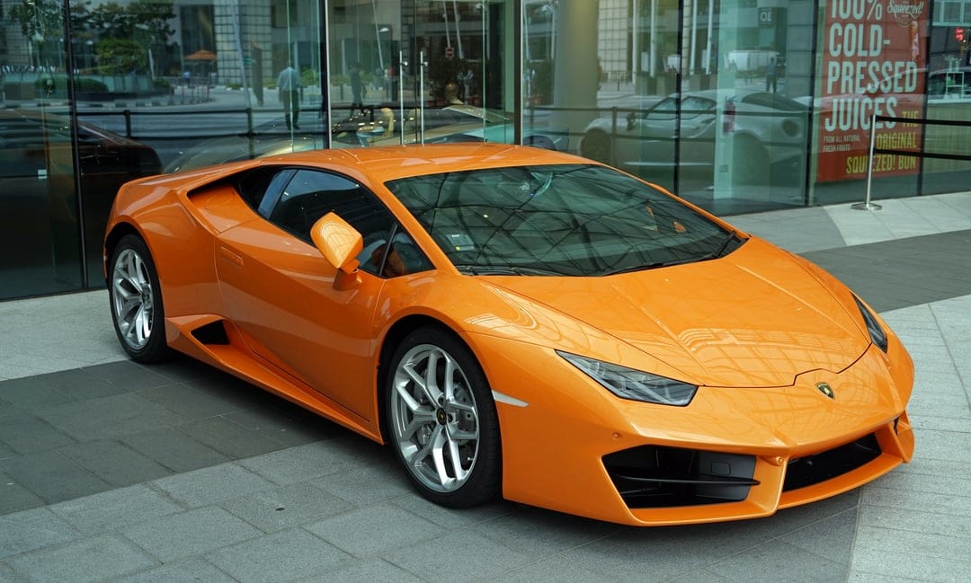 Orange Lamborghini Huracan parked on a stone walkway in front of a modern glass office building at daytime.