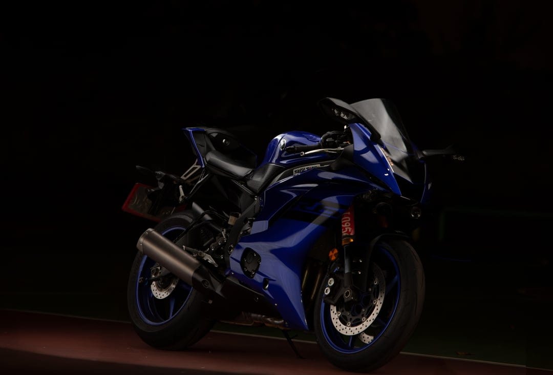 Yamaha R6 motorcycle with blue fairings and gold front forks isolated against a dark, moody background.