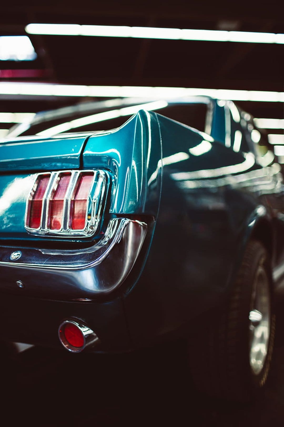 Teal Ford Mustang rear view with triple vertical taillights and a polished chrome bumper in soft lighting.