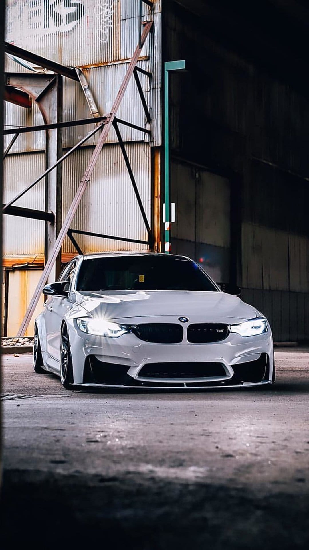 White BMW M3 sports car with aggressive body lines parked against corrugated metal in a low-angle urban shot.
