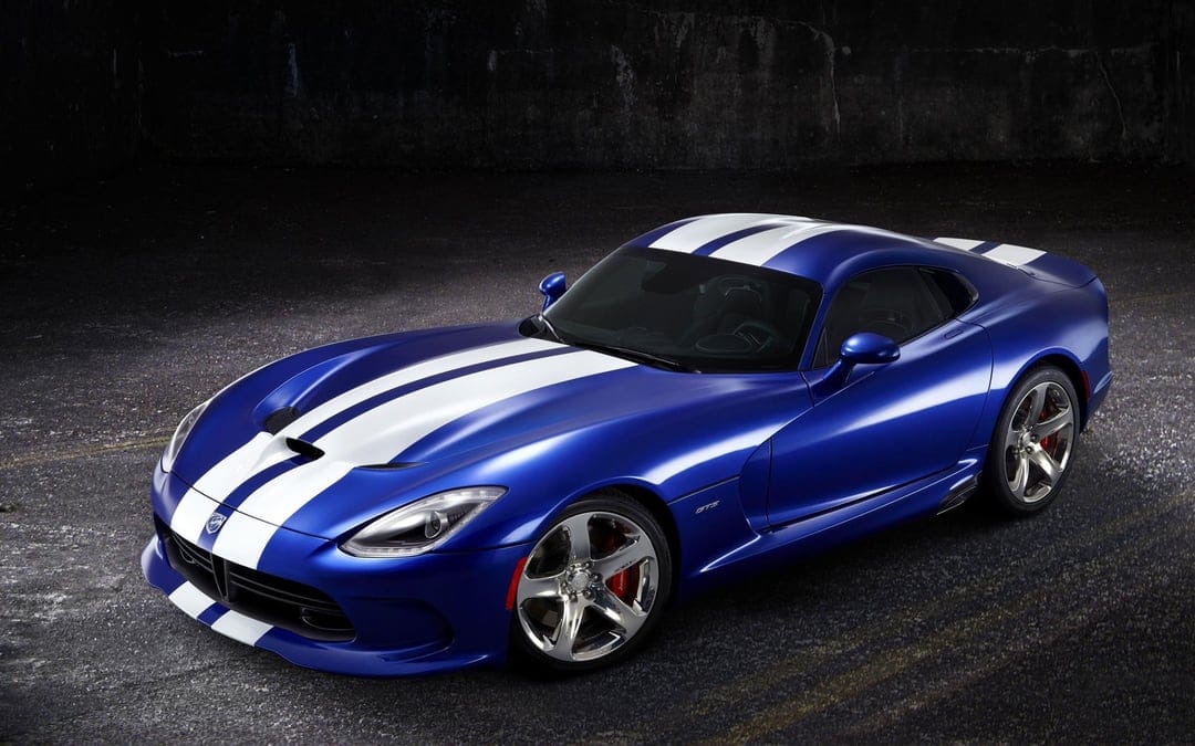 Blue Dodge Viper GTS with white racing stripes and chrome wheels parked on dark asphalt in a moody setting.
