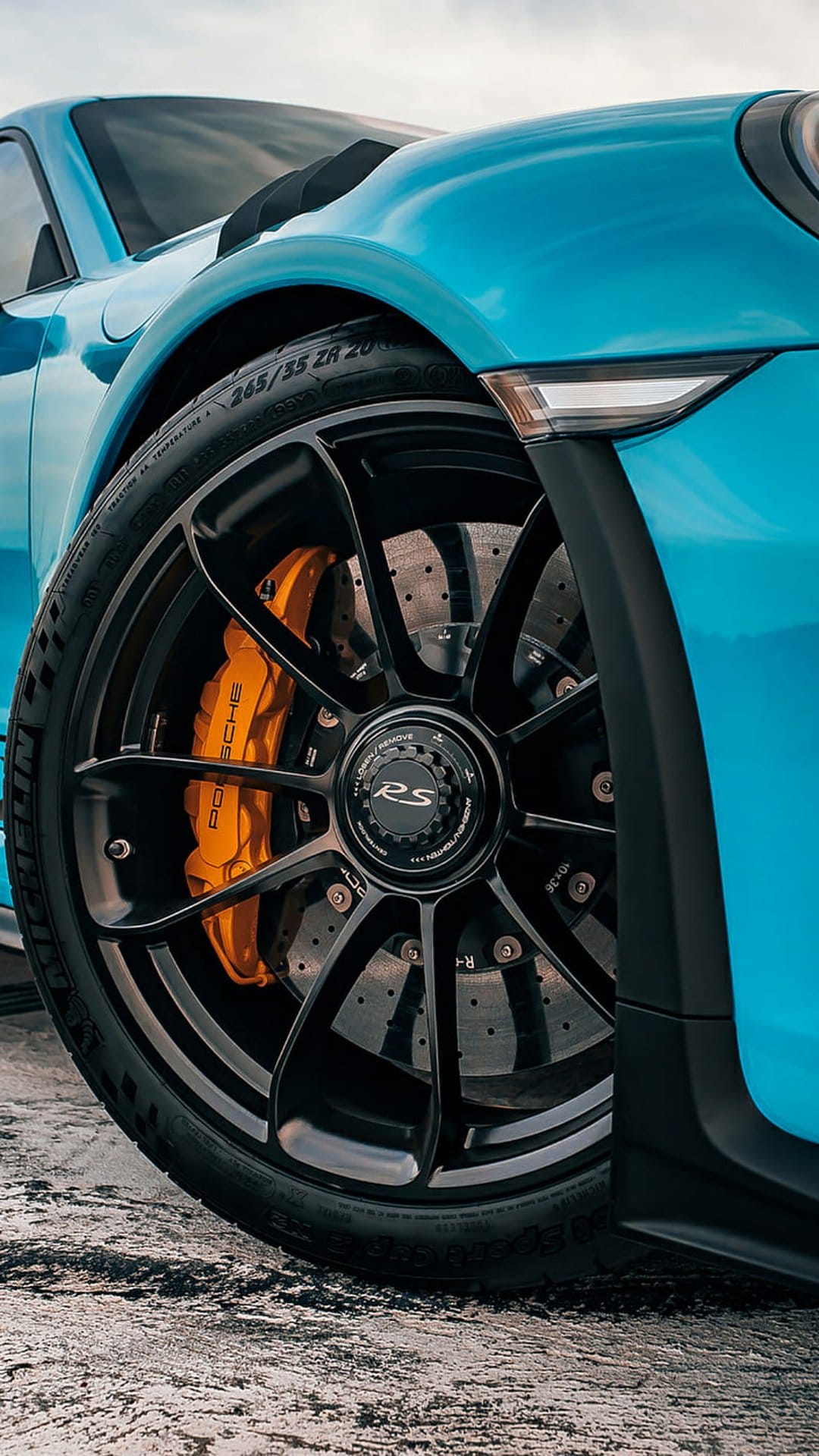 Blue Porsche 911 RS wheel featuring a black rim, orange brake caliper, and ventilated disc on a Michelin tire.