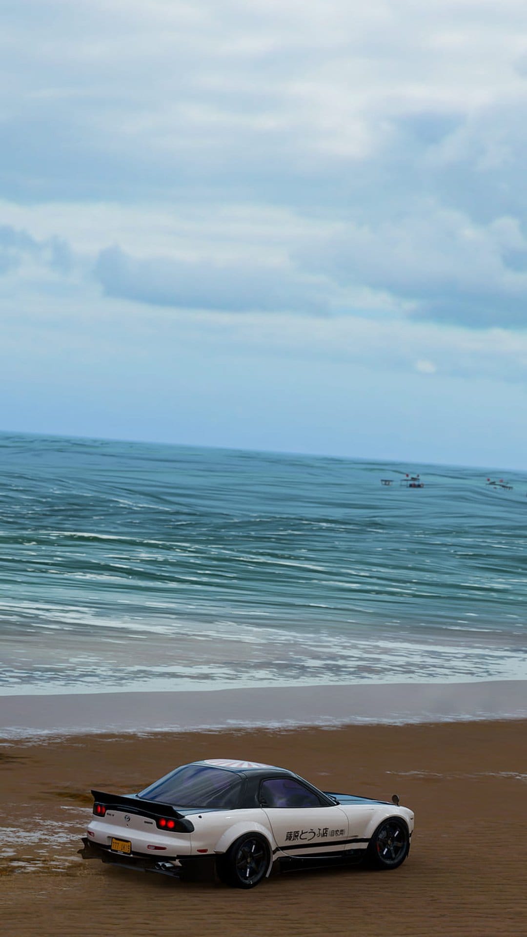 White Mazda RX-7 sports car parked on a sandy beach with rolling ocean waves and a cloudy sky in the background.