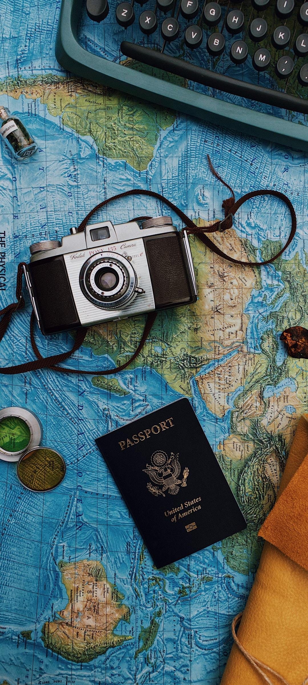 Green vintage typewriter and analog camera arranged on an antique world map with a leather journal and passport.