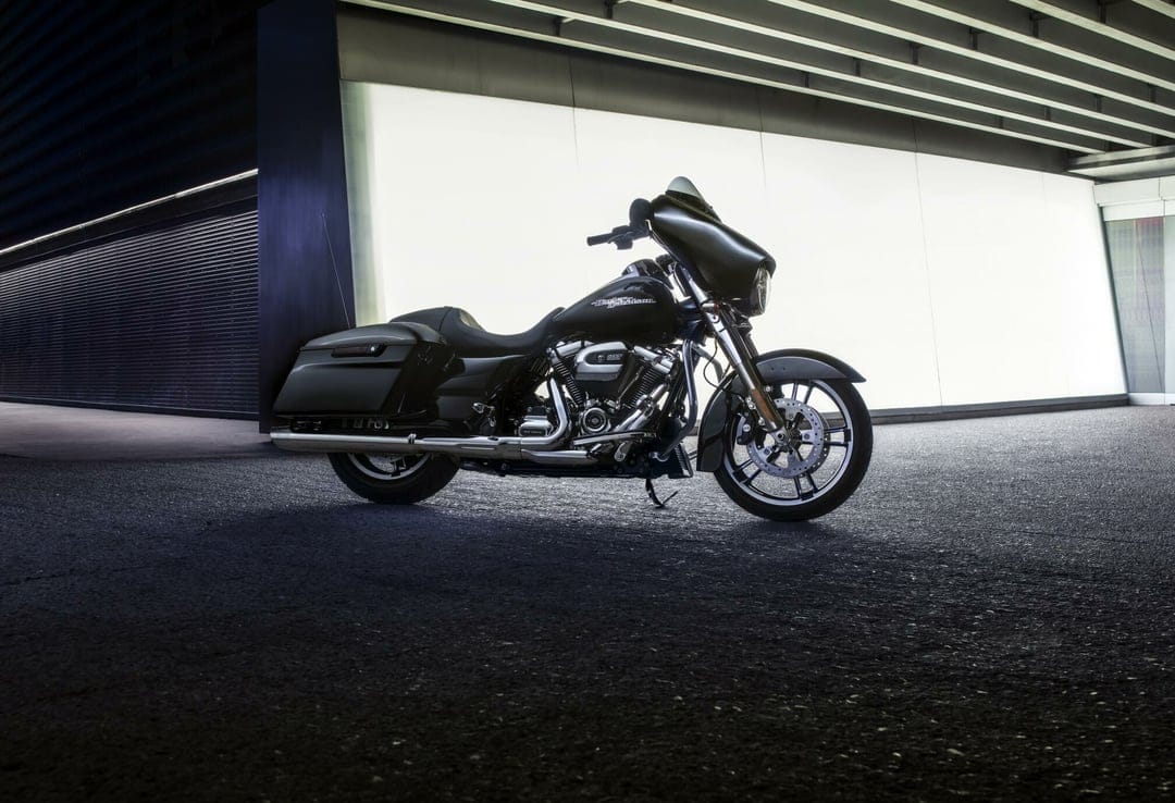 Black Harley-Davidson motorcycle parked in front of a glowing white wall in a modern industrial garage.