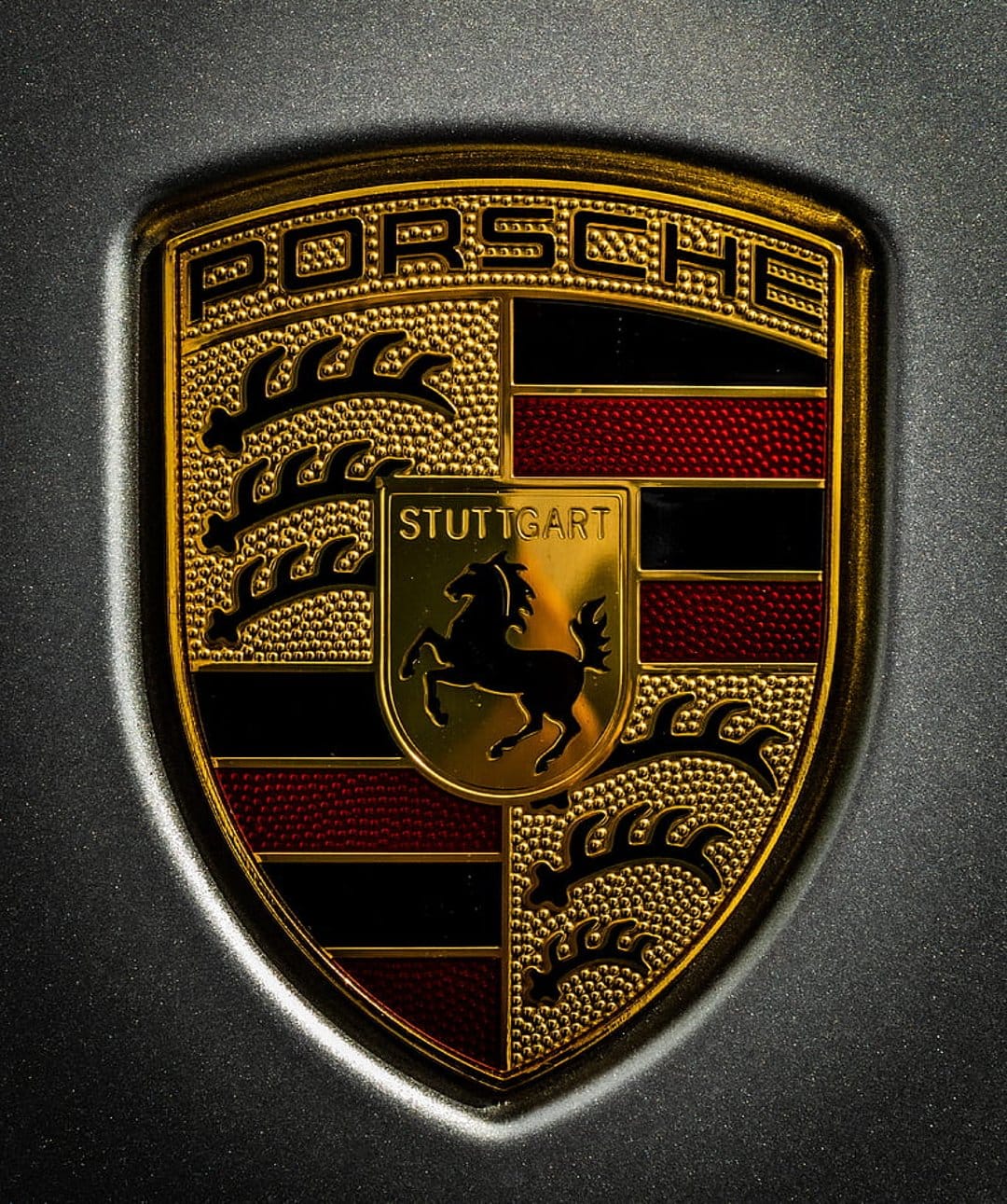 Porsche gold shield emblem with a black stallion, red stripes, and antlers, showing detailed metallic textures.