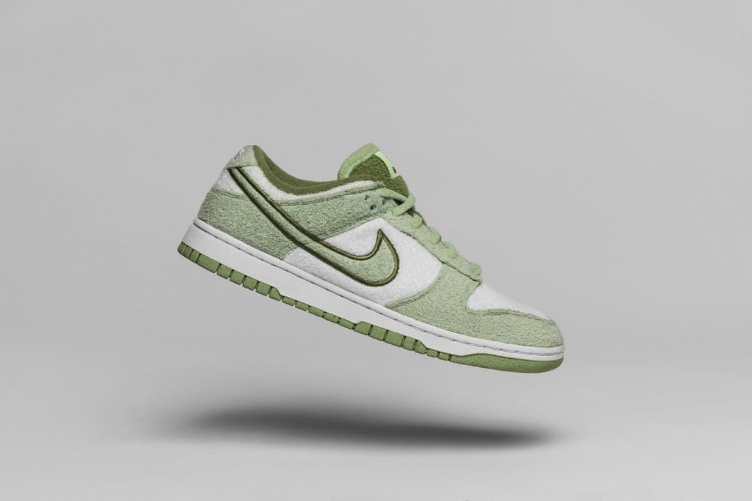 Nike Dunk Low sneakers with green plaid fabric and white leather overlays floating against a gray background.