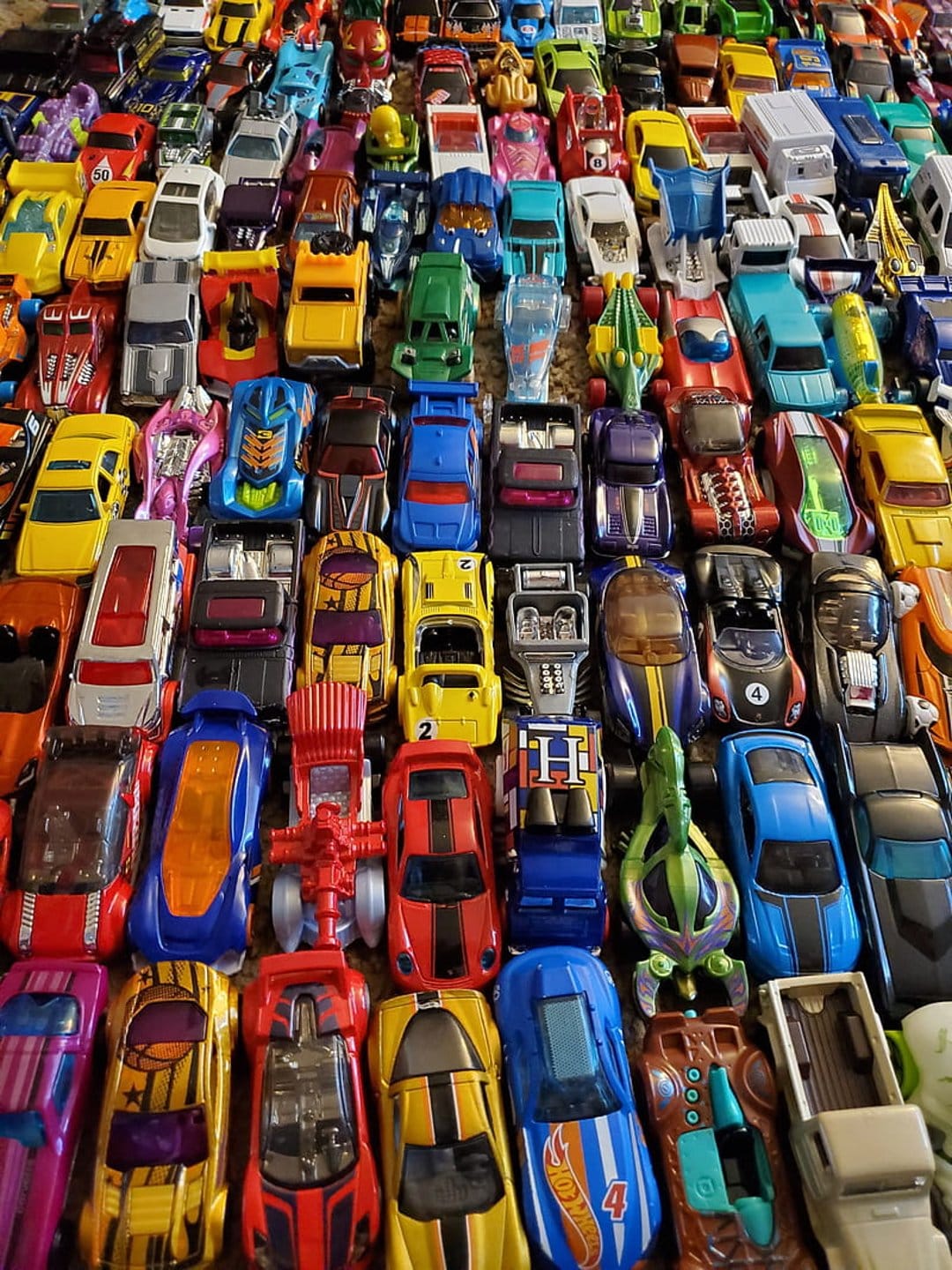 Rows of colorful die-cast toy cars in a vertical grid, showing diverse miniature vehicle models and race cars.