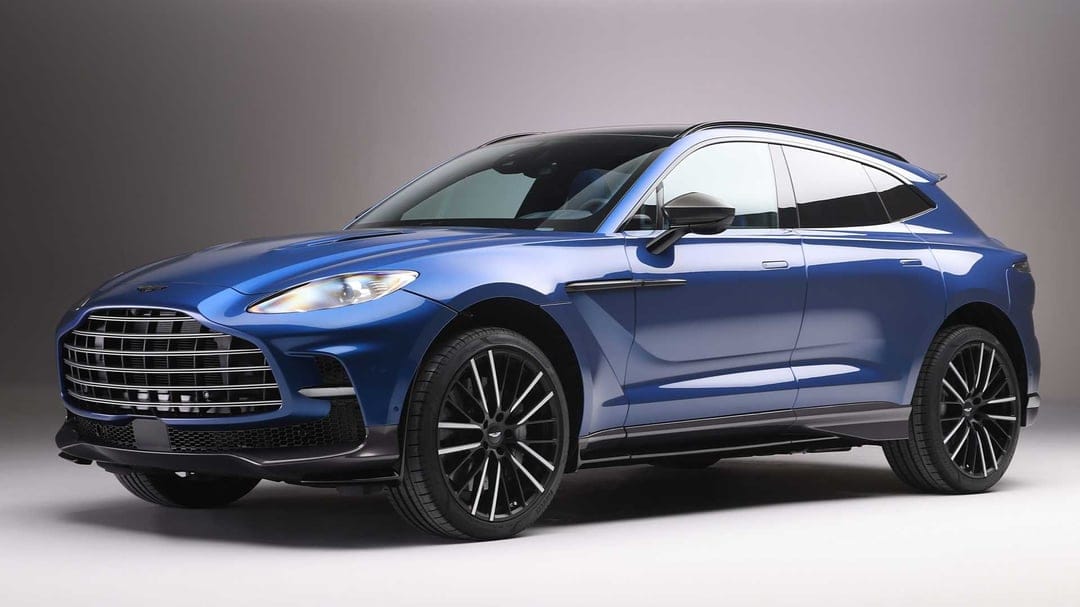 Metallic blue Aston Martin DBX707 luxury SUV parked in a studio with soft lighting and black alloy wheels.