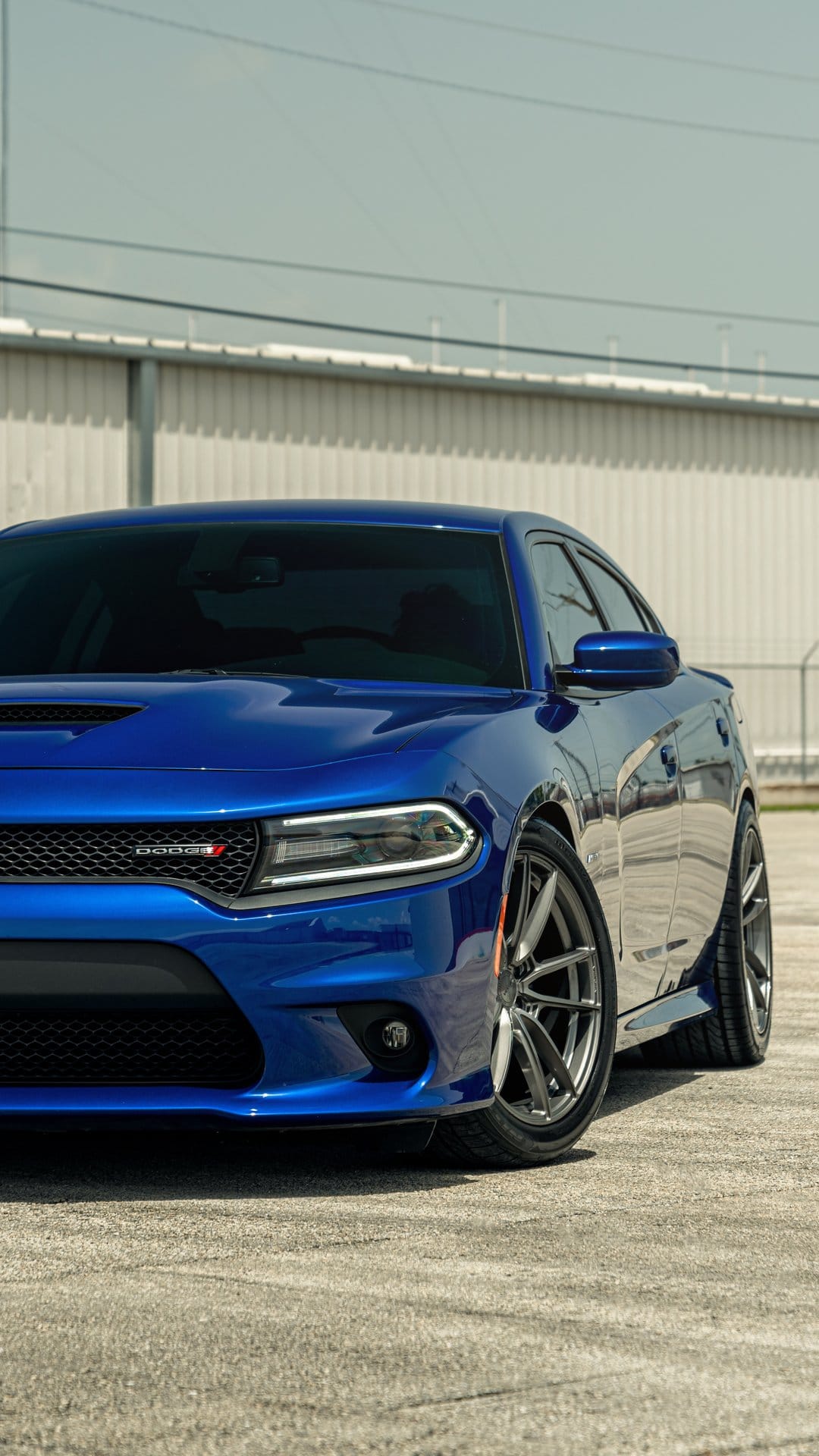 Front view of a blue Dodge Charger with LED headlights and custom multi-spoke wheels on a concrete lot.