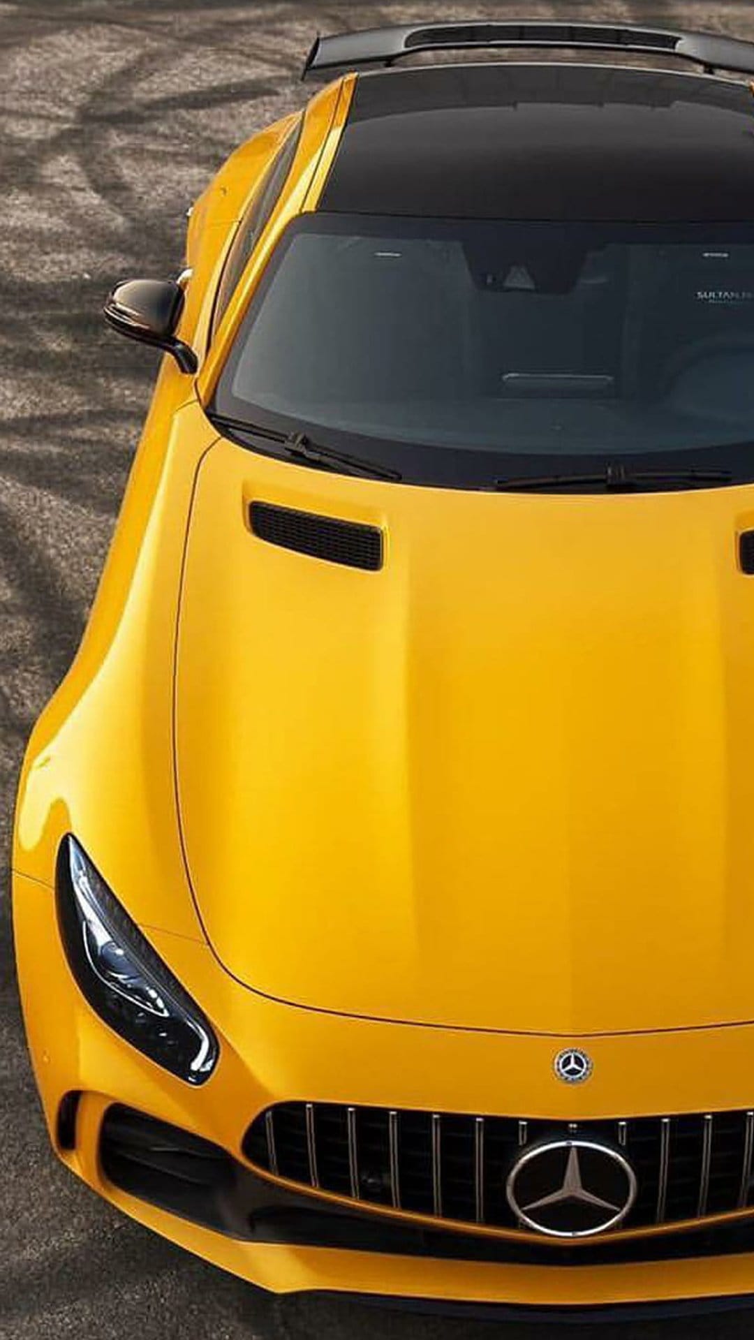 Yellow Mercedes-AMG GT R coupe viewed from above on a textured gray pavement with dark shadows and a black spoiler.