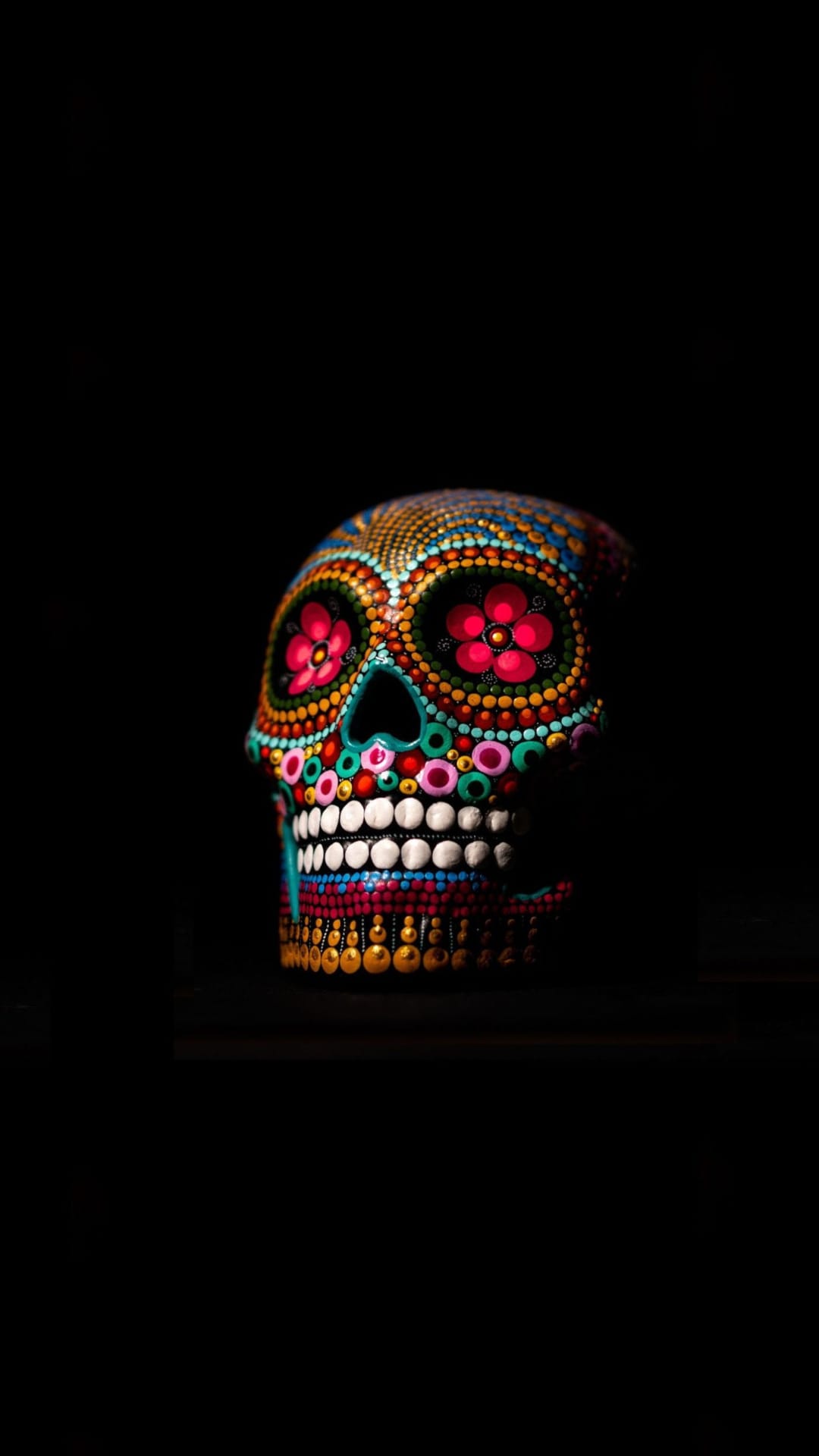 Sugar skull decorated with pink and yellow floral dot patterns on a solid black background in a vertical view.