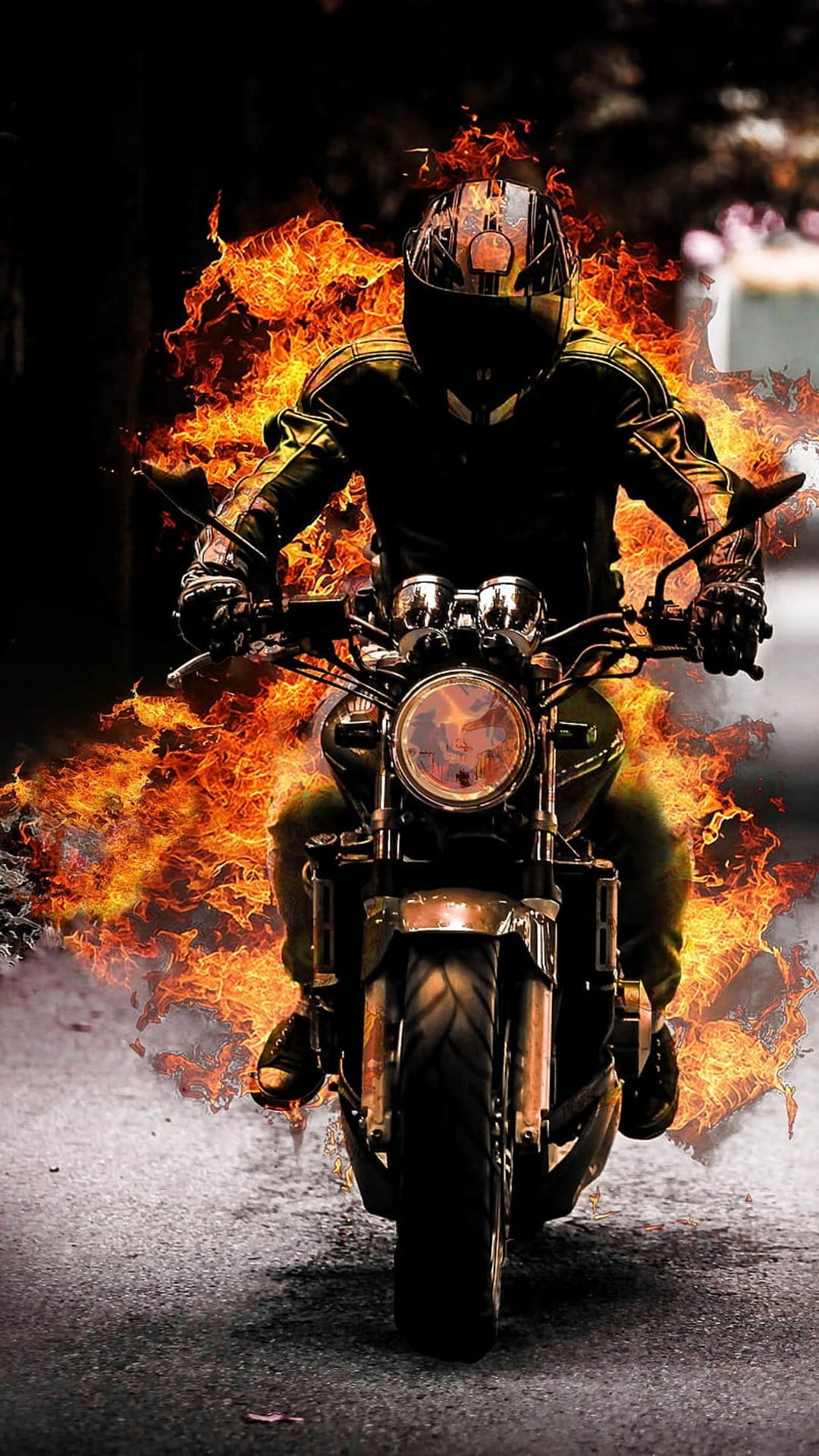 Motorcyclist wearing black gear rides a bike engulfed in orange flames on a dark asphalt road at night.