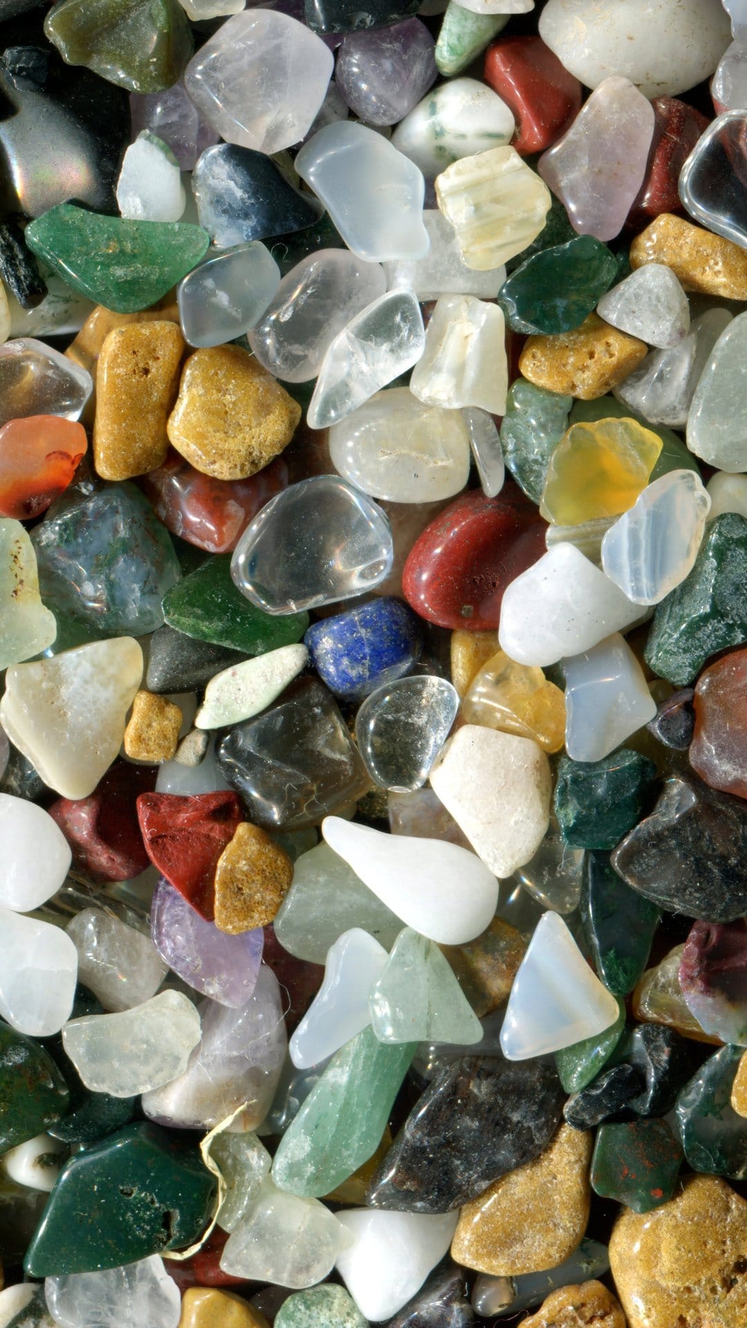 Polished gemstones in varying colors like green, red, and blue form a dense, textured mineral arrangement.
