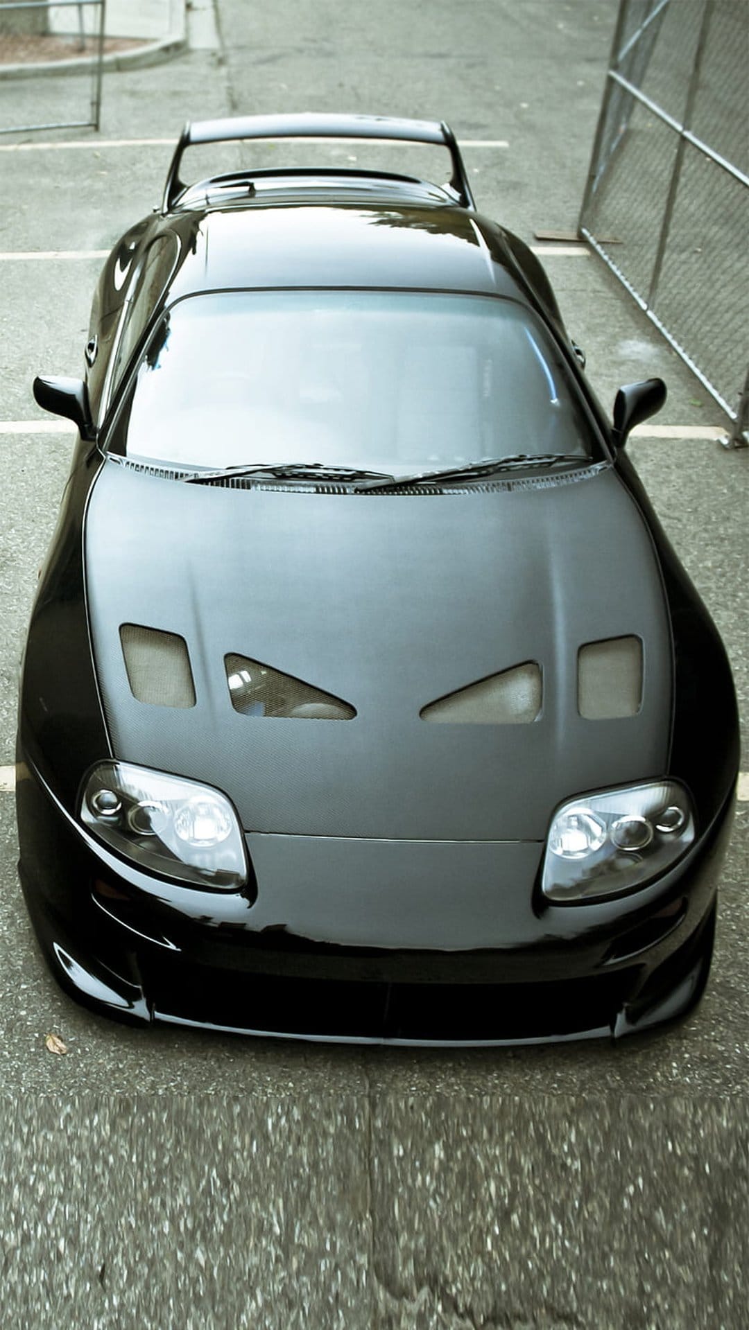 Black Toyota Supra with custom hood vents and a large rear spoiler parked on asphalt from a high angle.