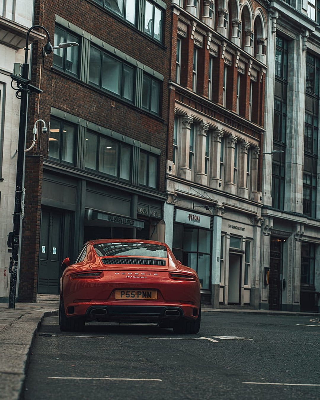 Red Porsche 911 parked on a wet cobblestone street in London next to classic brick and stone buildings.