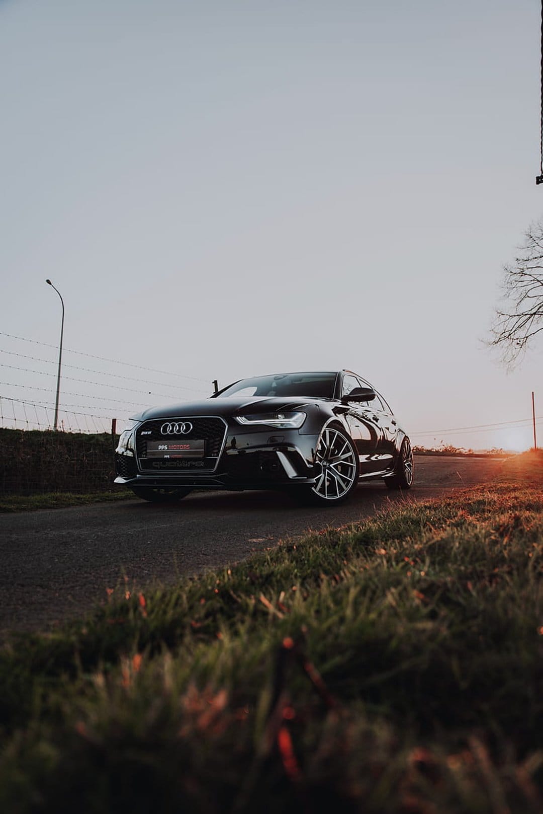 Black Audi RS6 Avant parked on an asphalt road at sunset with golden light hitting its aggressive front bumper.