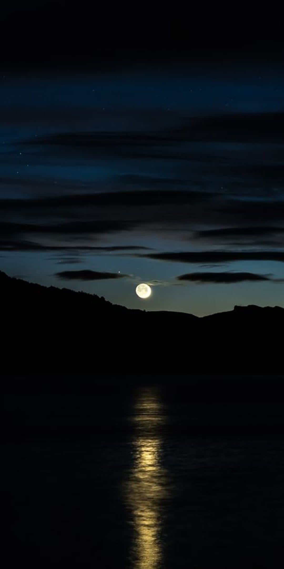 Full moon glowing above dark hills with a bright white light reflecting on the calm surface of a midnight lake.