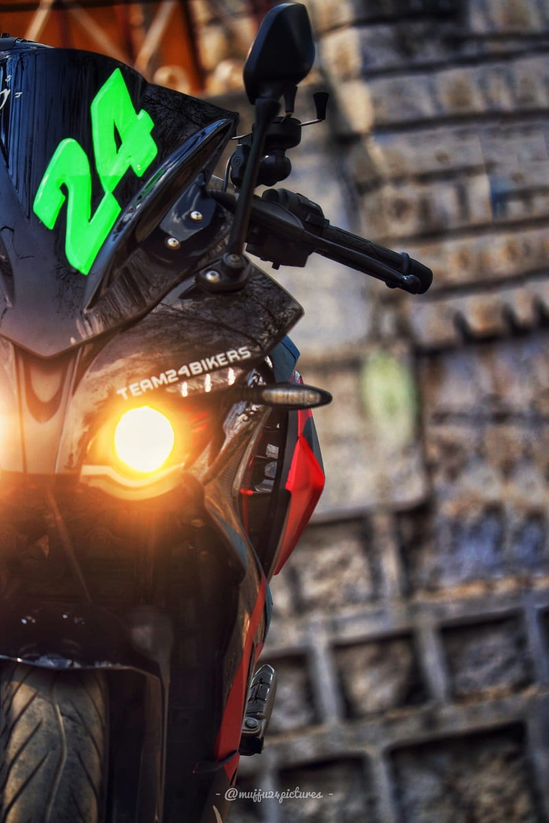 Black motorcycle fairing with a green 24 sticker and a bright orange illuminated headlight against a stone wall.