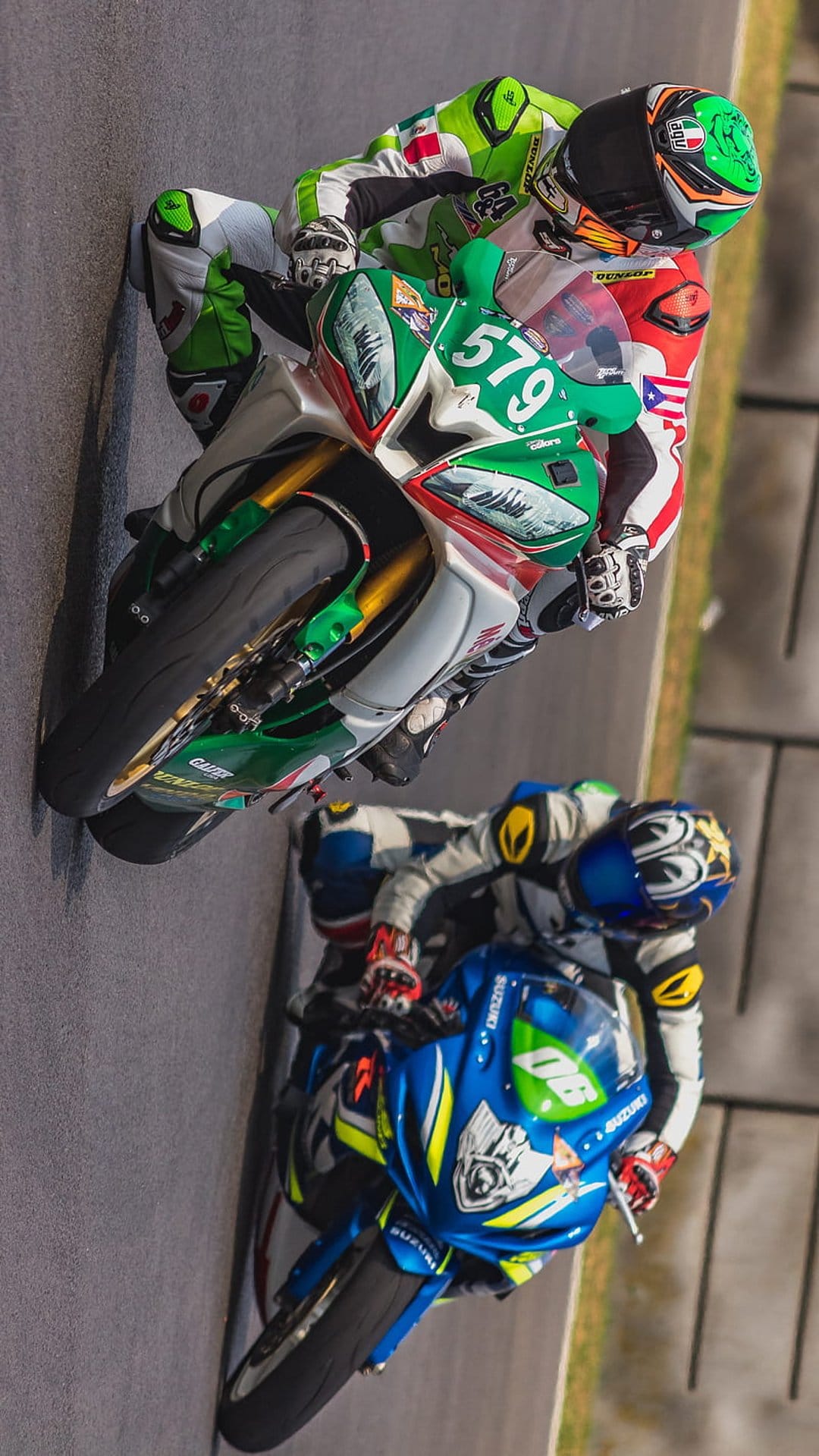 Two motorcycle racers in colorful suits lean low into a racetrack corner during a high-speed competitive event.