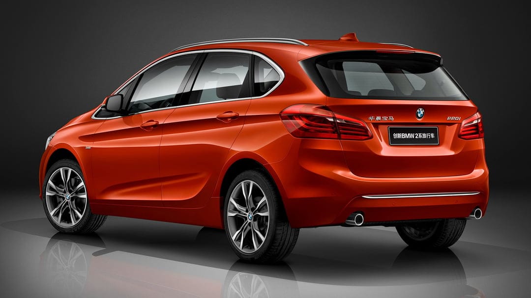 Rear view of a metallic orange BMW 2 Series hatchback on a reflective studio floor with dark background.