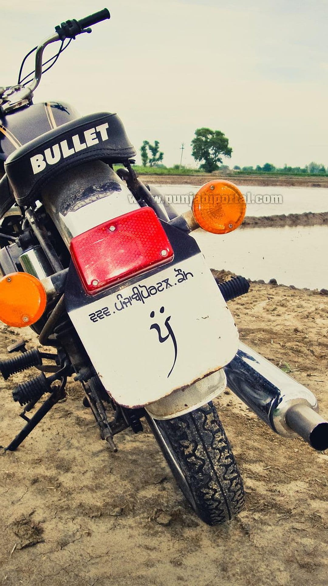 Bullet motorcycle rear featuring a Punjabi license plate and tail light on a dirt path under a cloudy sky.
