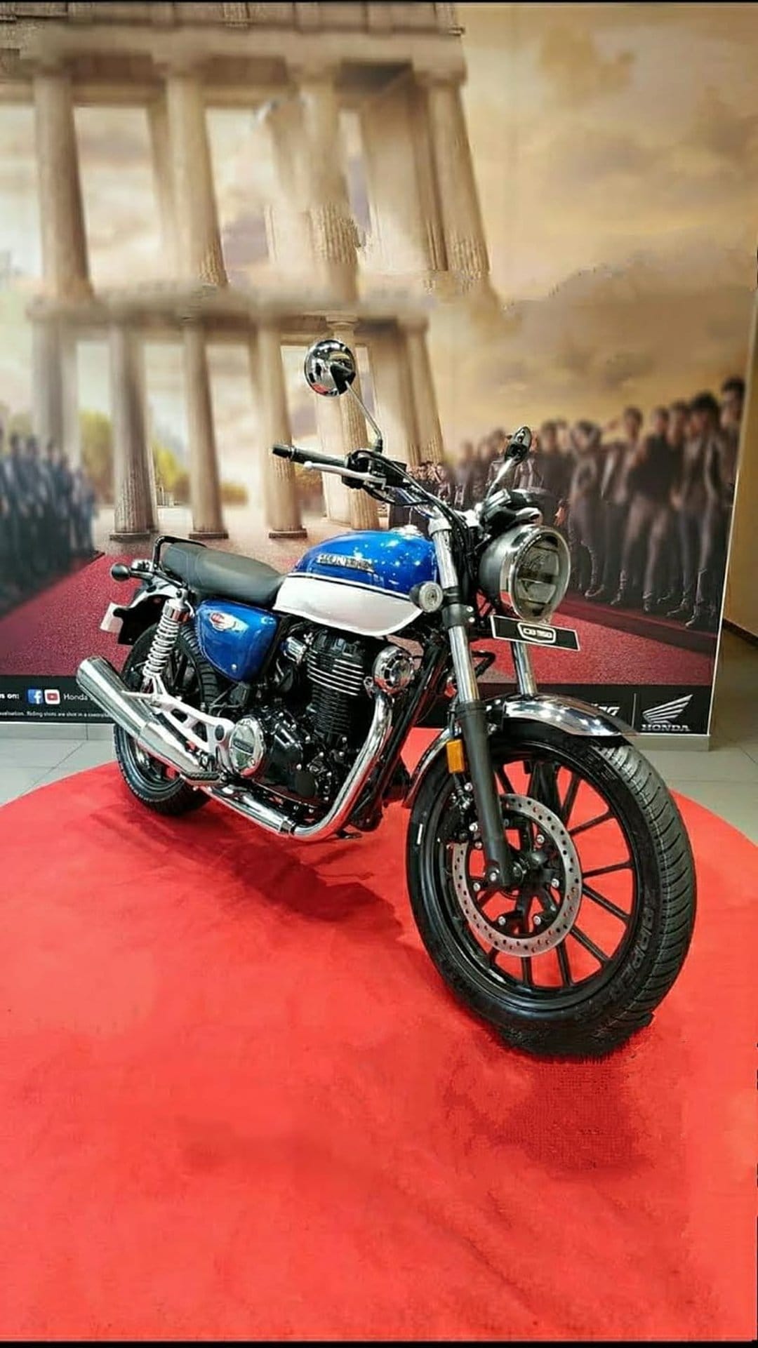 Honda motorcycle with blue and white paint on a red carpet inside a grand hall with blurred crowds behind it.