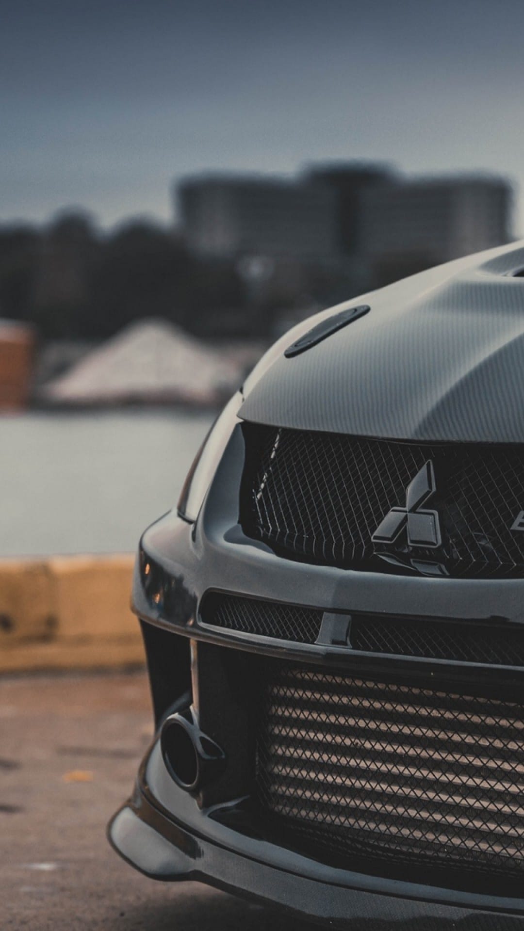 Black Mitsubishi Lancer Evolution front grille and carbon fiber hood in a moody, industrial setting.
