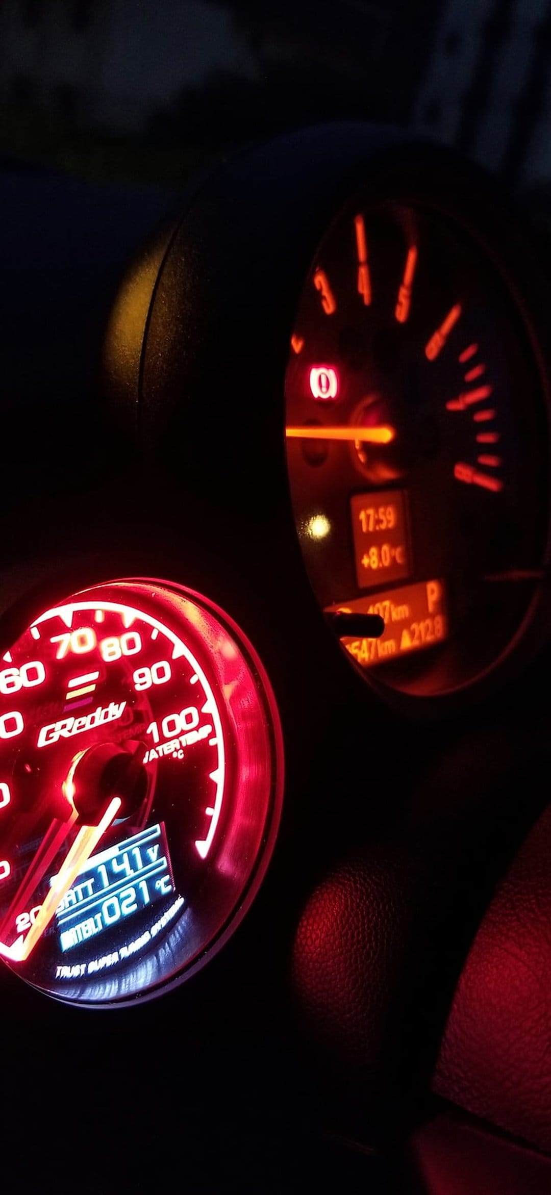 Red illuminated GReddy water temperature gauges and digital dashboard displays glow inside a dark car interior.