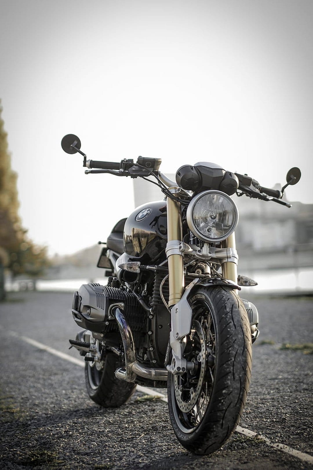 BMW R nineT motorcycle with gold forks and round headlight parked on an asphalt road with a blurred background.