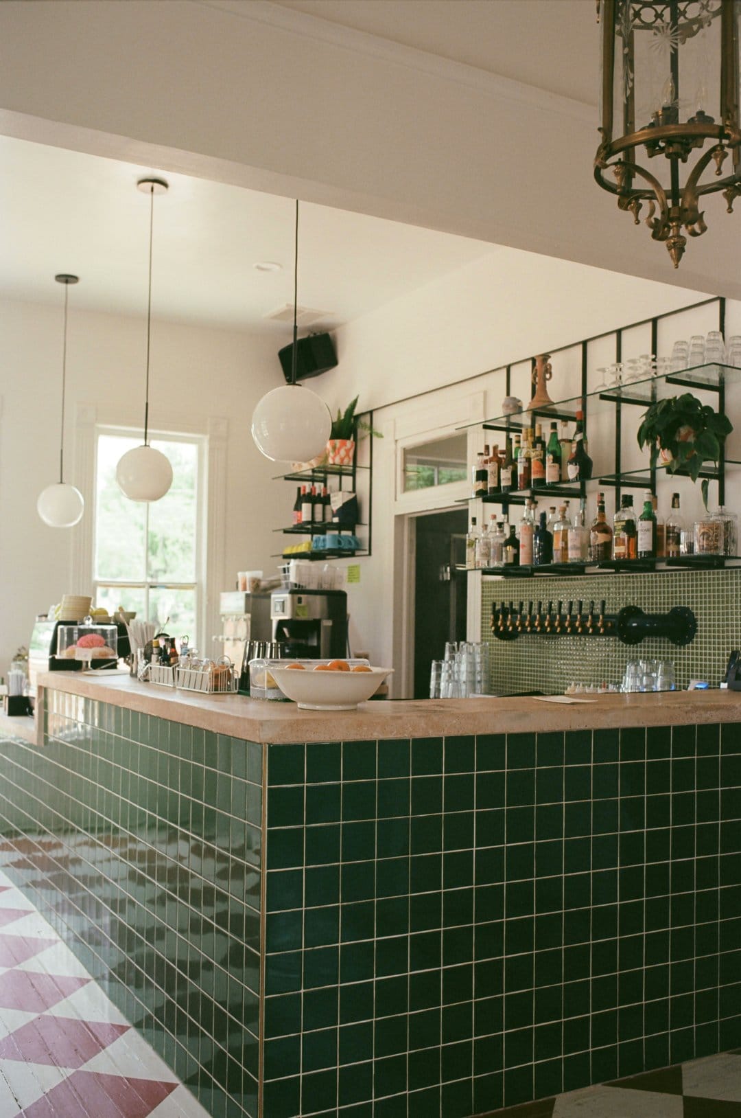 Emerald tiled bar counter with a light wood surface beneath hanging pendant lights in a stylish cafe interior.