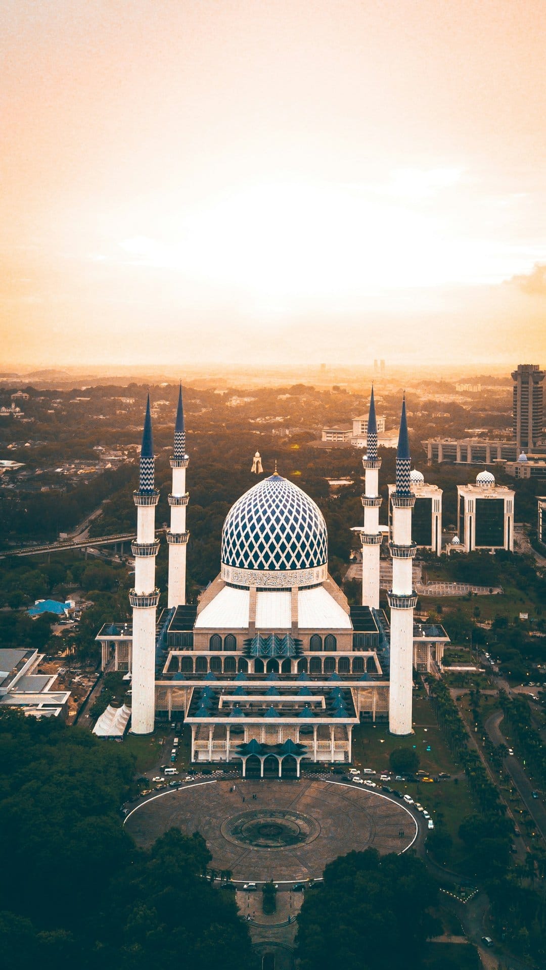 Intricate blue and white mosque dome with tall minarets overlooking a hazy cityscape during a golden sunrise.