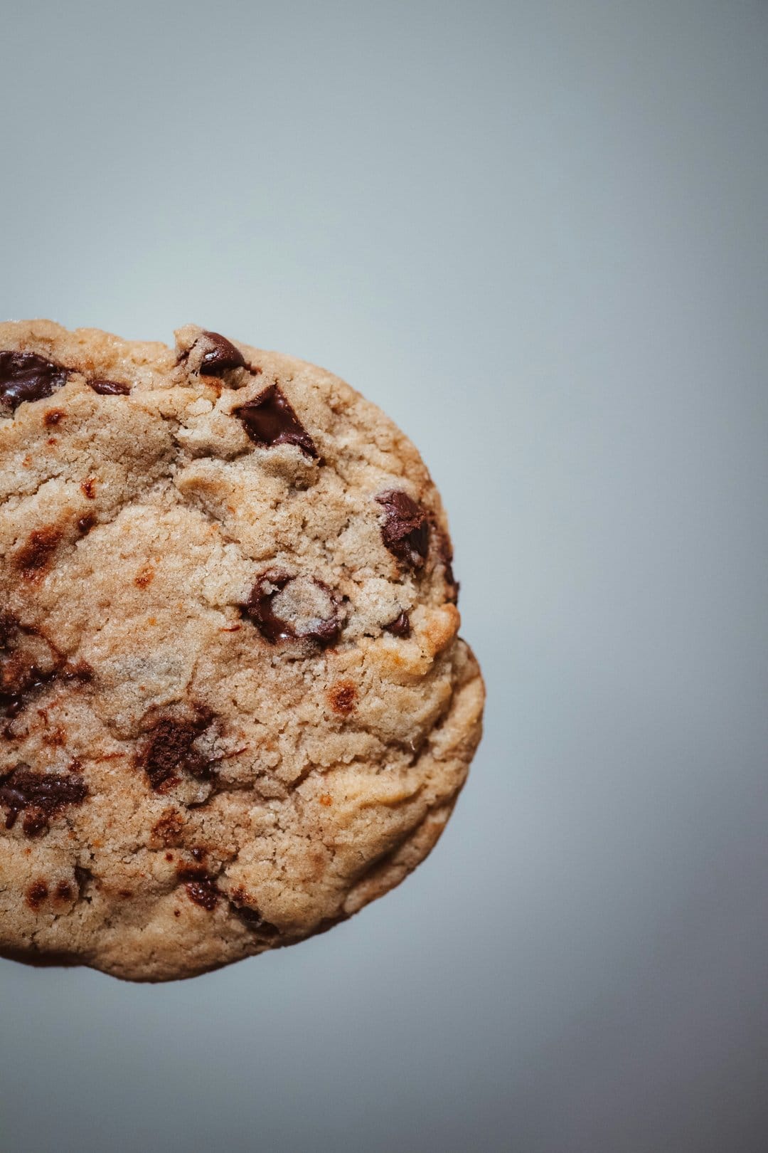 Freshly baked chocolate chip cookie with golden crinkled edges and melted dark chips on a soft background.