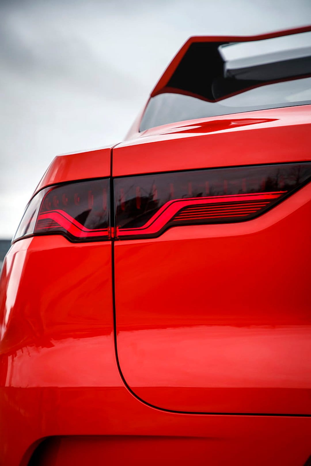 Jaguar F-Type red LED taillight glows against glossy crimson bodywork with soft ambient sky reflections.
