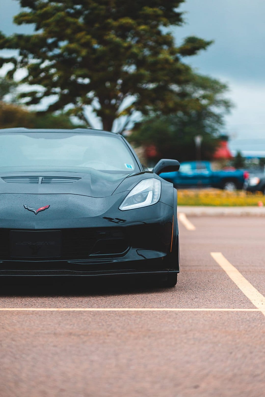 Black Chevrolet Corvette front end parked on asphalt with yellow lines under a gloomy overcast sky.