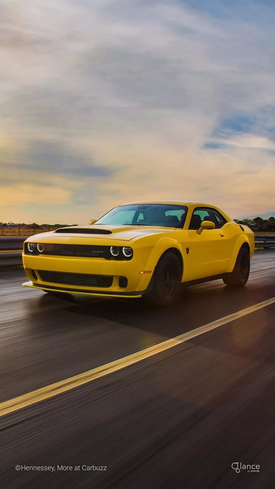 Yellow Dodge Challenger SRT Hellcat muscle car speeding on a race track under a dramatic, cloudy sky.