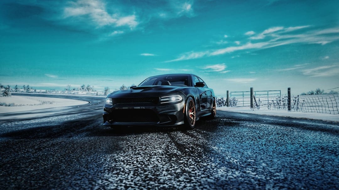Black muscle car with bronze rims on a wet snowy road under a dramatic teal winter sky with soft clouds.