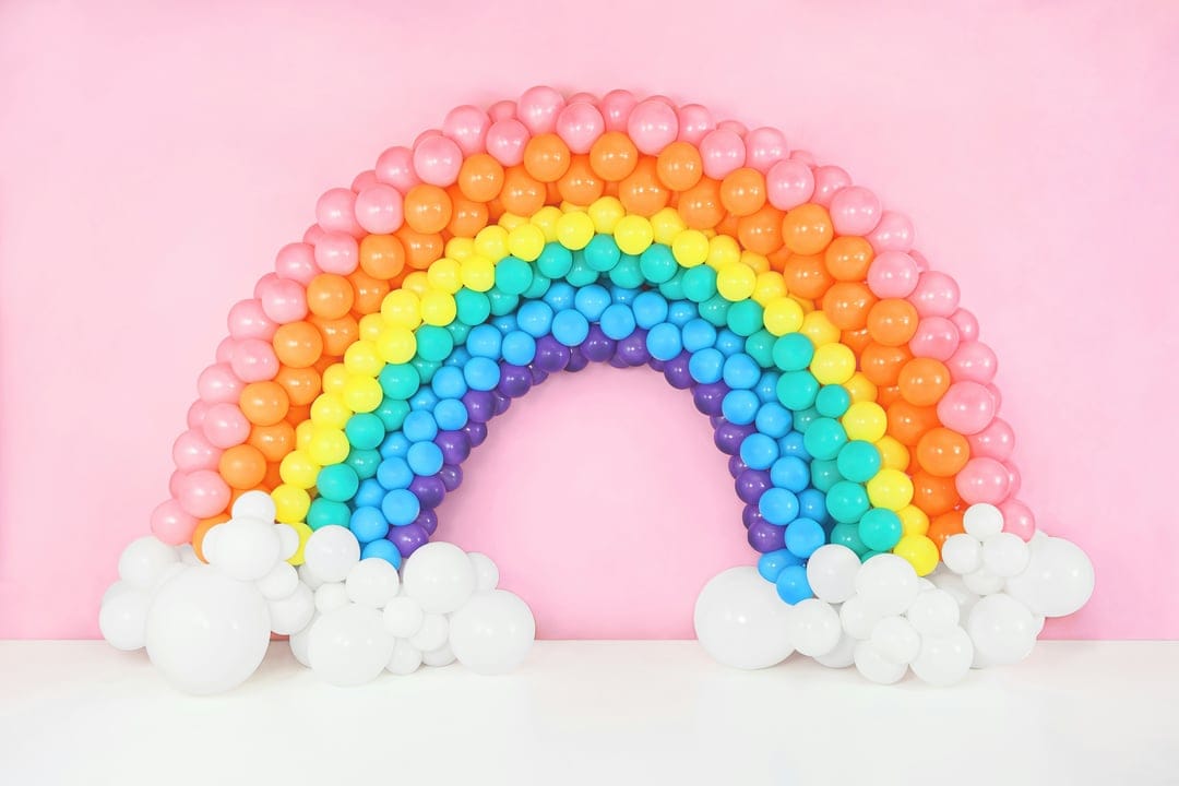 Multicolored balloon arch curves over white clusters, creating a festive display with saturated primary tones.