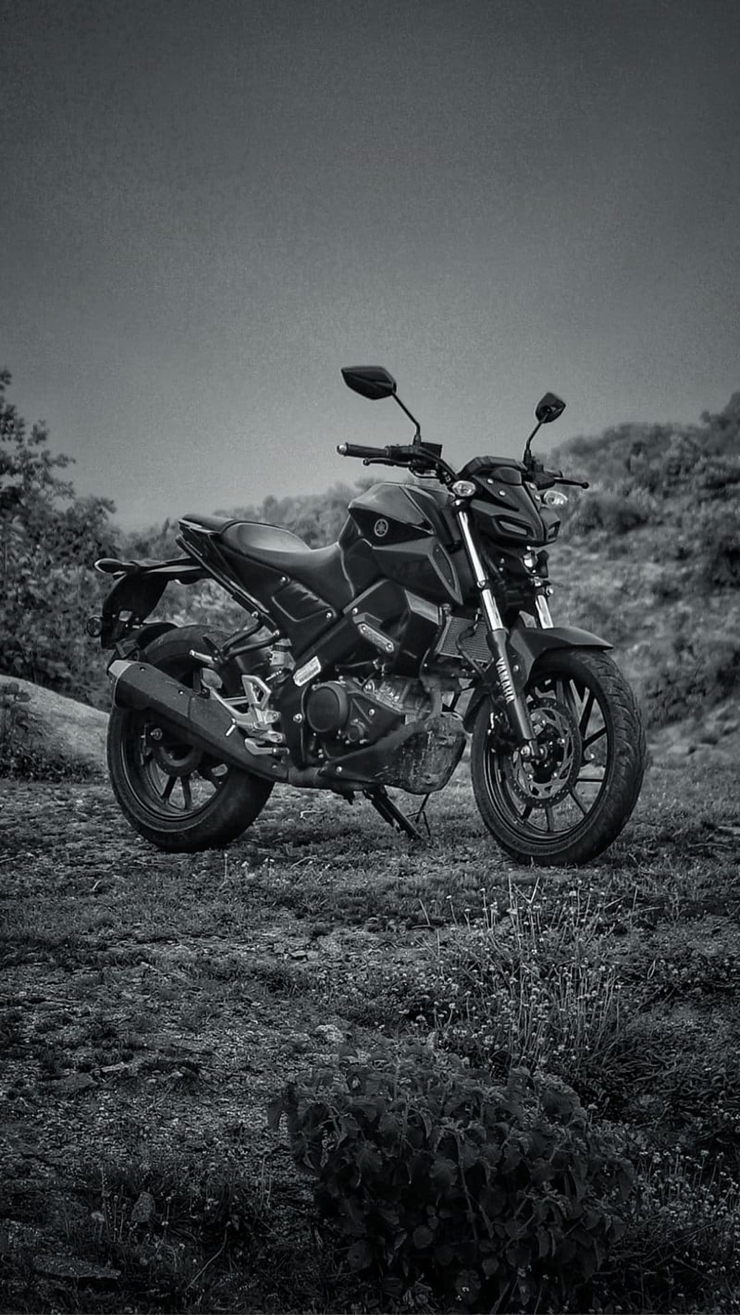 Black Yamaha motorcycle parked on a grassy hillside in a side-profile view with a monochrome photography style.