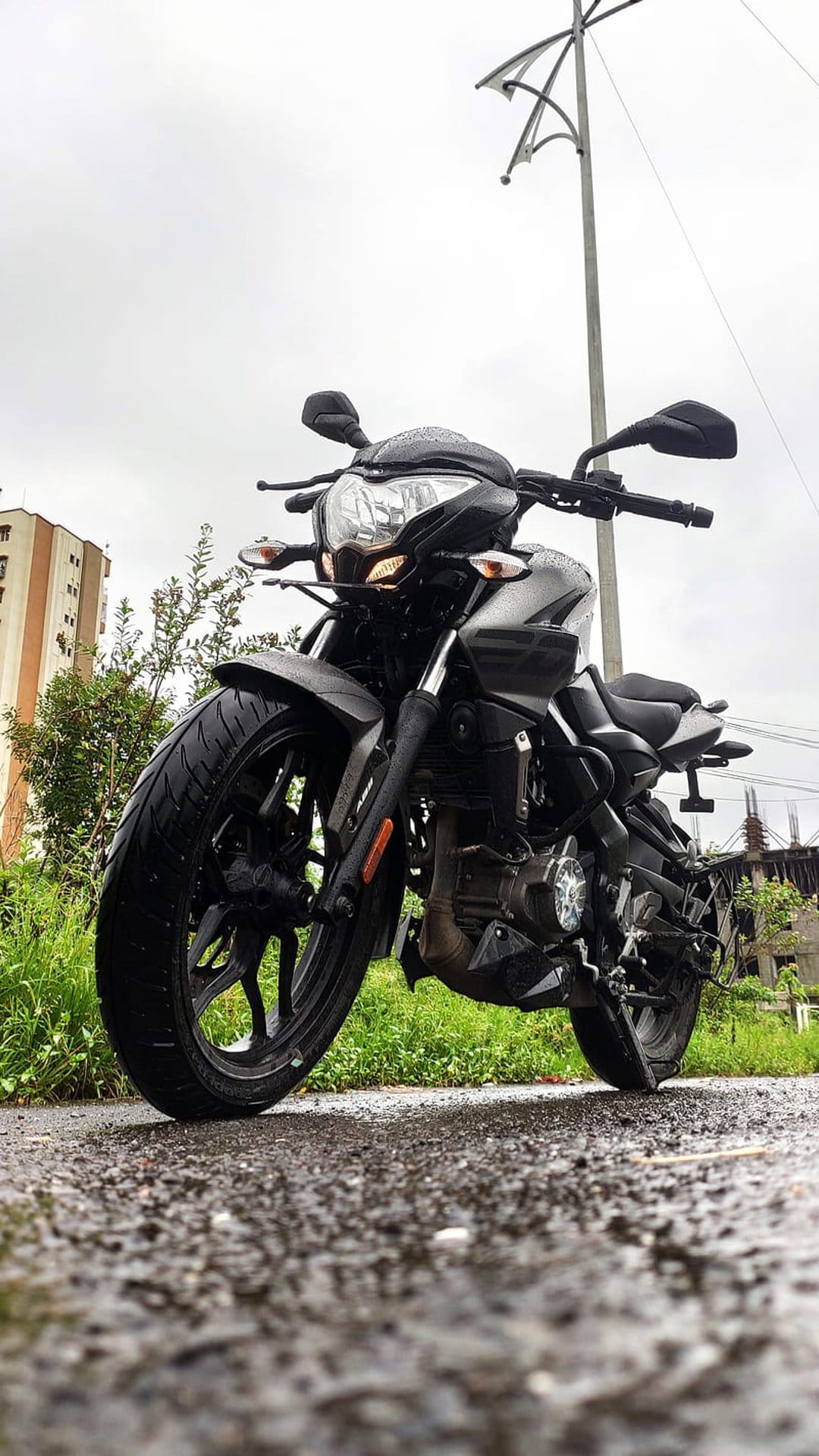 Dark motorcycle parked on a wet gravel road with a close-up on the front tire under a cloudy, overcast sky.