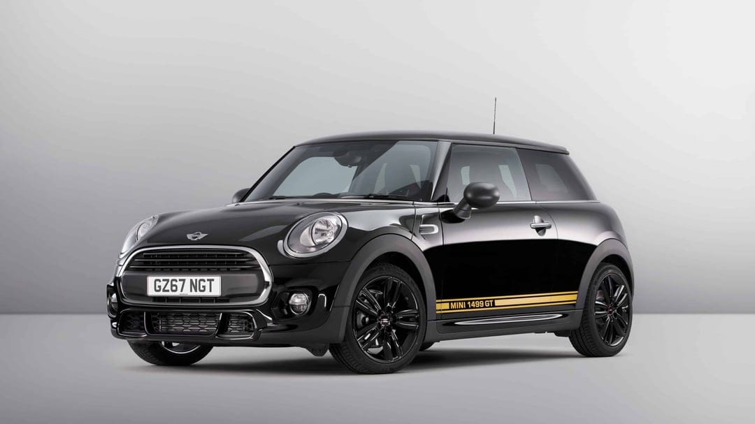 Black Mini 1499 GT hatchback with yellow side stripes and black rims in a minimalist grey studio setting.