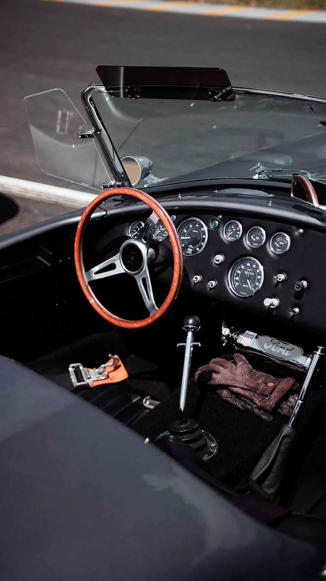 Polished wooden steering wheel and chrome gear shift inside a vintage car cockpit with brown leather driving gloves.