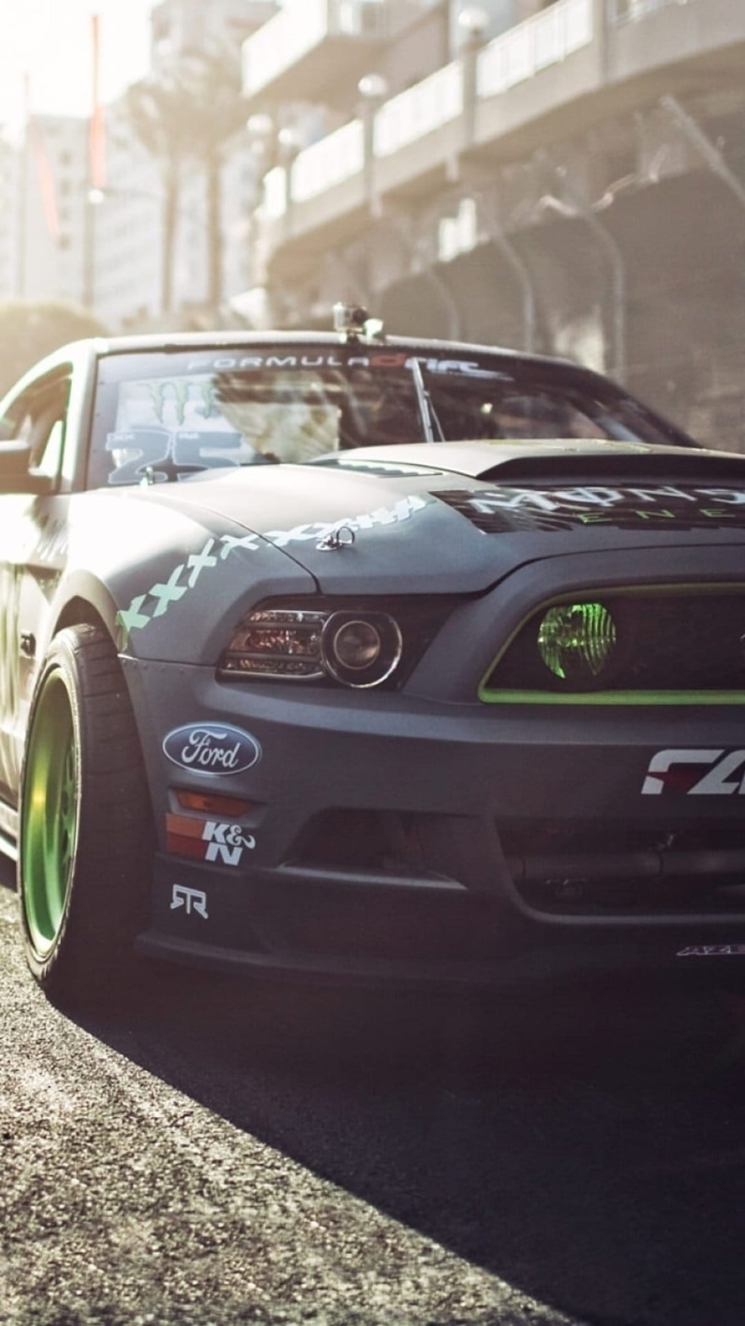 Ford Mustang drift car with matte black paint and neon green wheels parked at a low angle in bright sunlight.