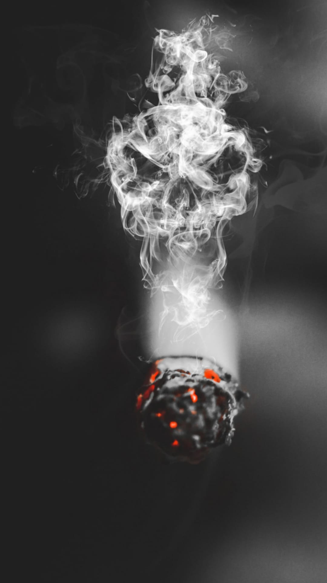 Human skull formed by white cigarette smoke rising from a glowing orange ember against a dark black background.