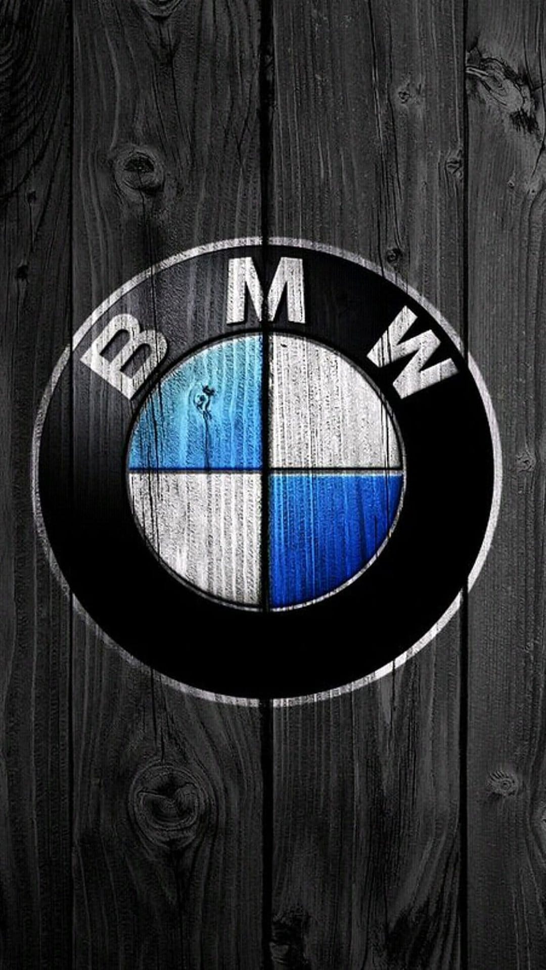BMW logo with blue and white quadrants mounted on a dark, vertically grained wooden plank with visible textures.