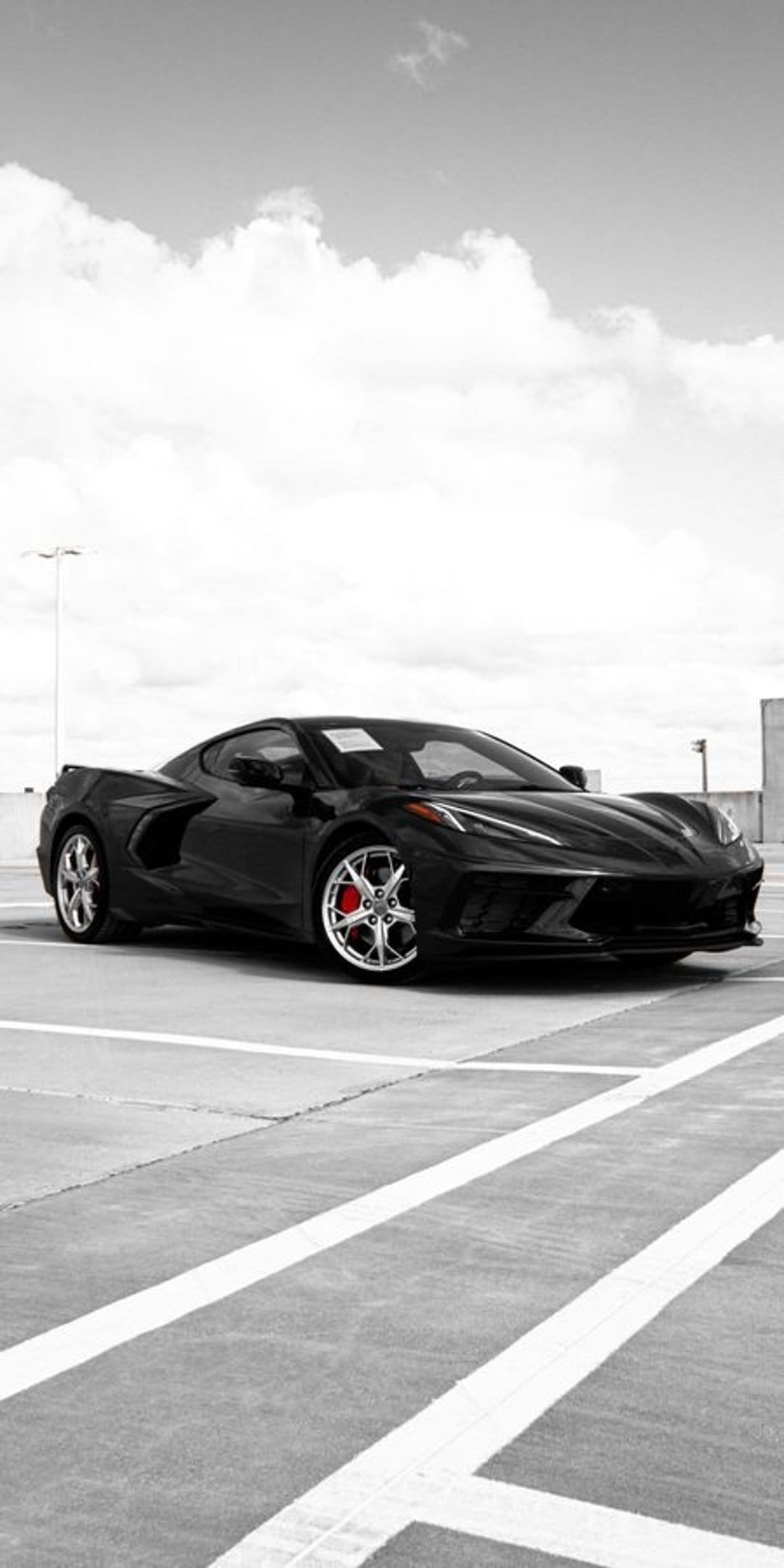 Black Corvette C8 parked on concrete under wispy clouds, featuring red brake calipers and a monochromatic finish.