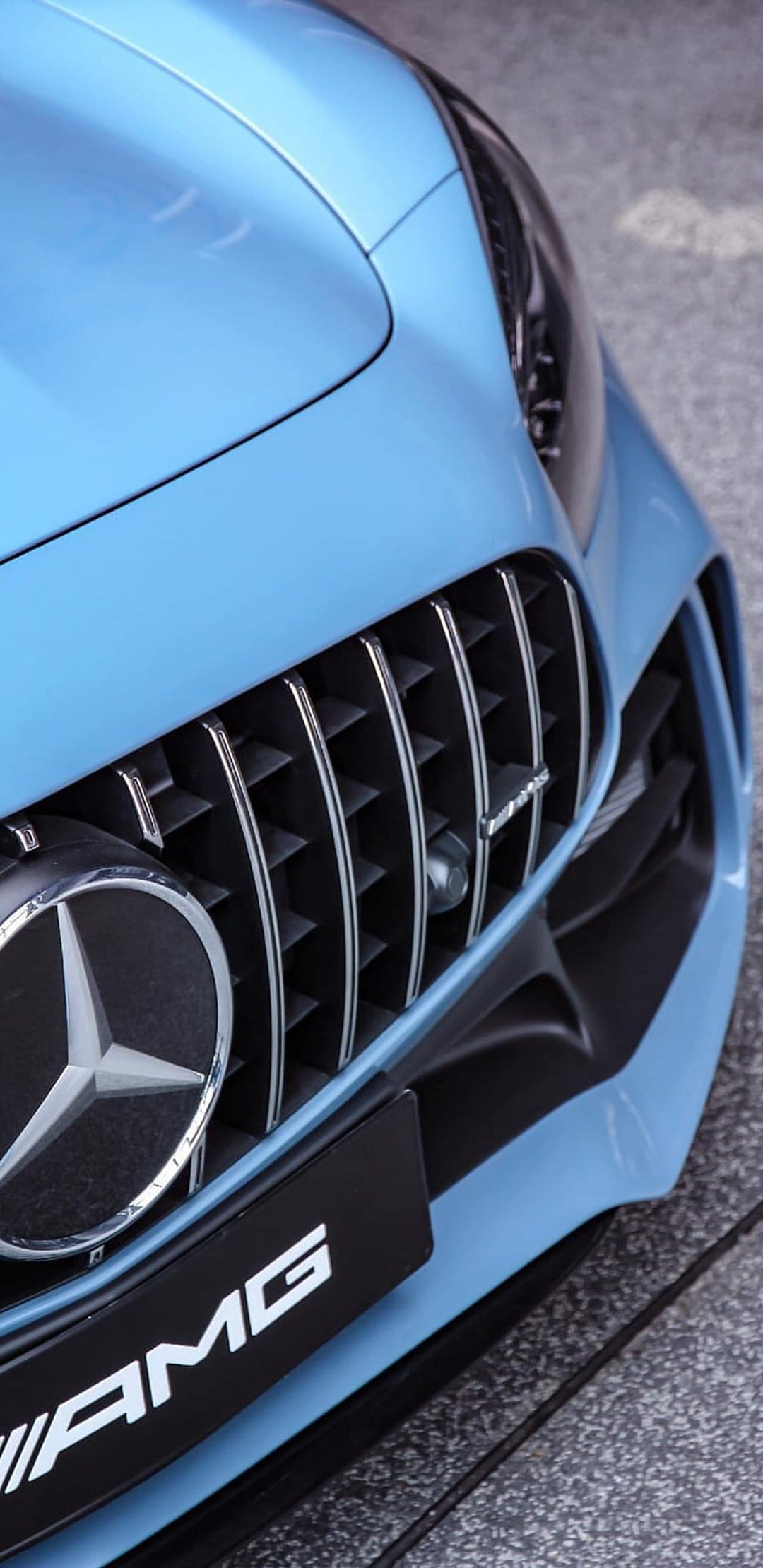 Mercedes-AMG GT front grille features vertical chrome slats and a silver star emblem on a light blue vehicle.
