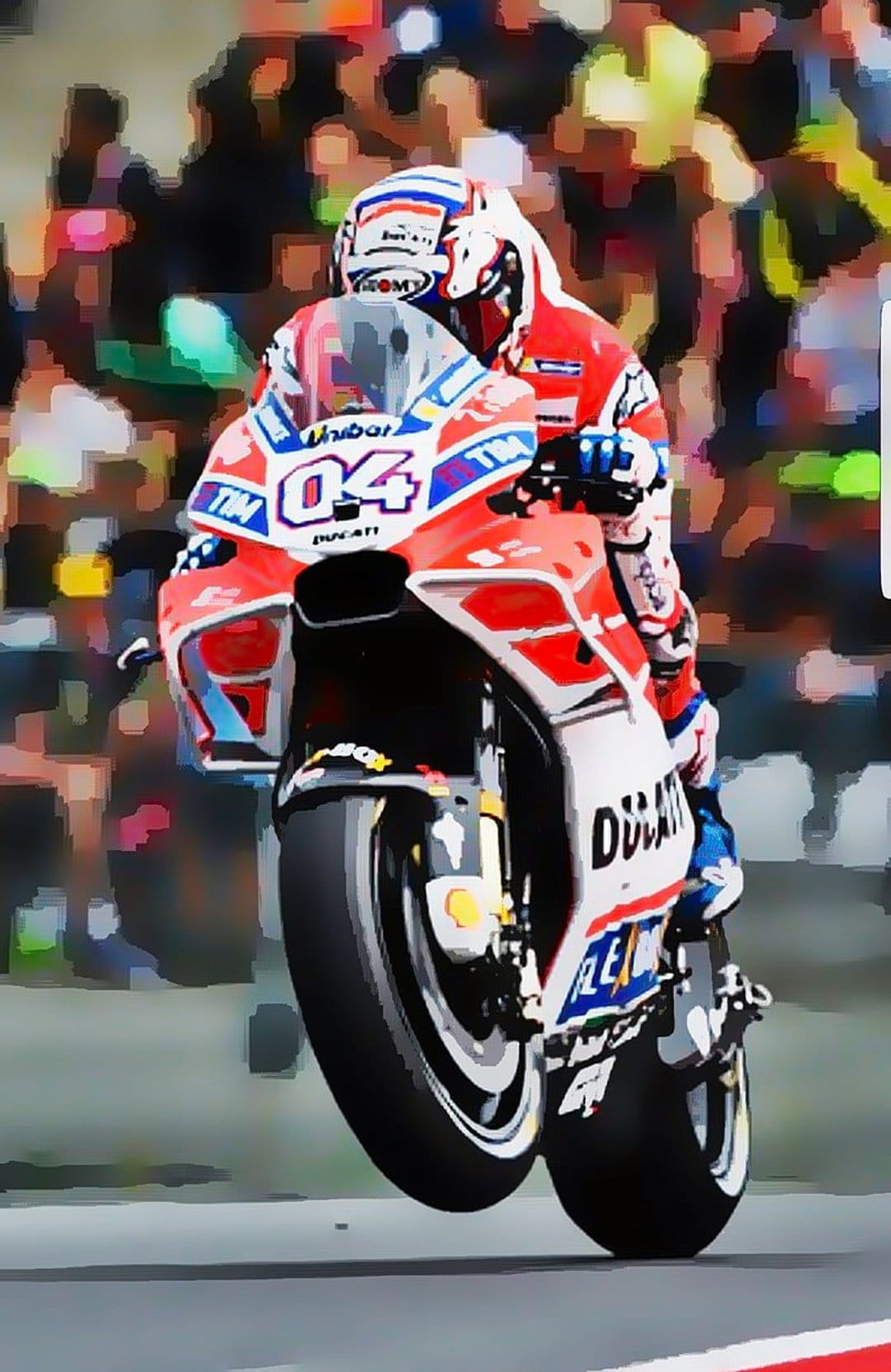 Ducati rider in red leathers performs a wheelie on a race track with motion blurred spectators in the background.