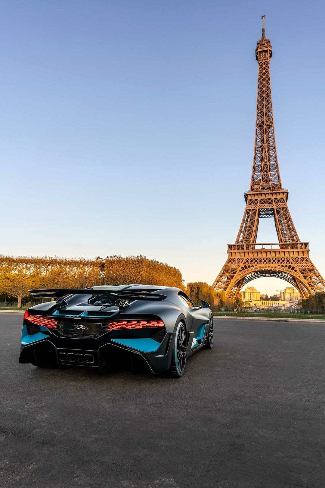 Matte black Bugatti Divo hypercar with blue accents parked in front of the Eiffel Tower at sunset.