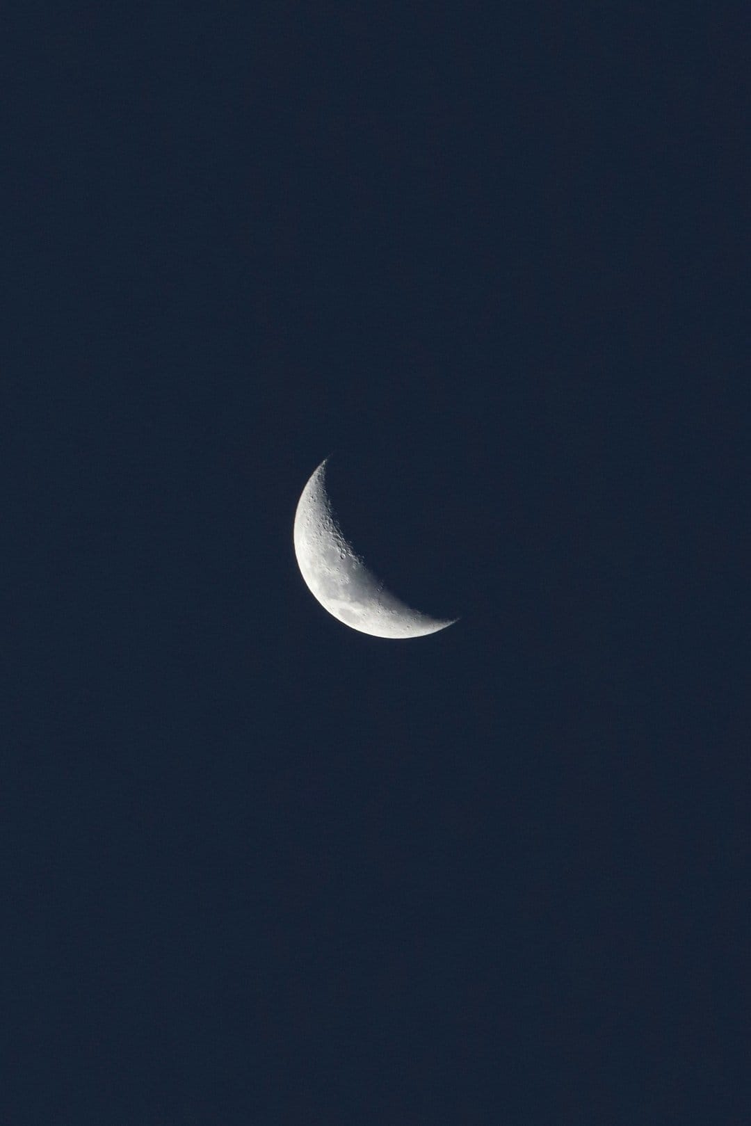 Waxing crescent moon with visible craters shines against a dark navy gradient sky in a vertical composition.